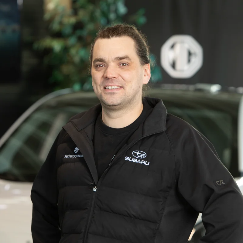 Person med langt hår står foran hvit bil innendørs.