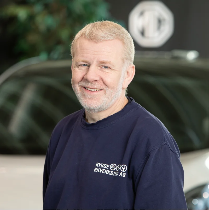 En mann med blondt hår står foran et hvitt kjøretøy.